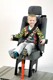 Boy smiling, sitting in HYBRID Seat, secured by integrated 3 point belt